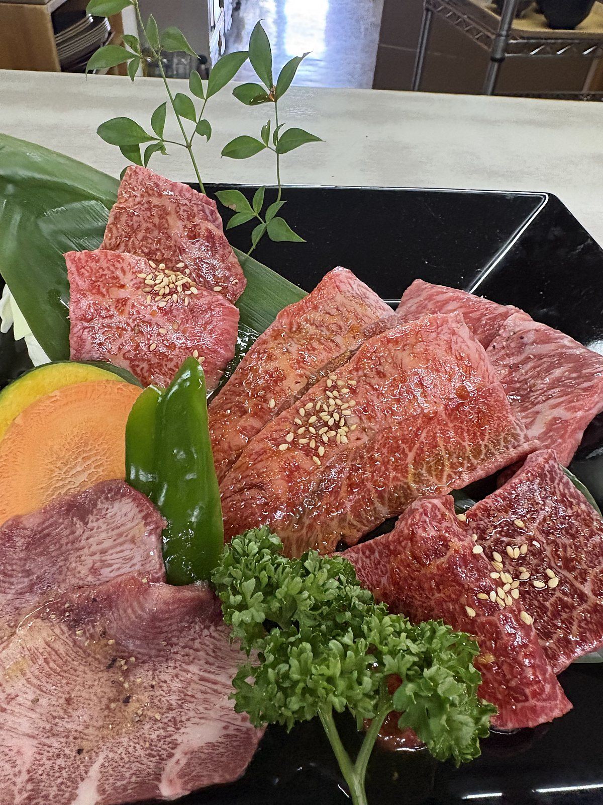 豊南焼肉の焼定 特上。黒い大皿に上タン、和牛カルビ、赤身などを笹の葉とともに盛り付けた焼肉定食の肉皿
