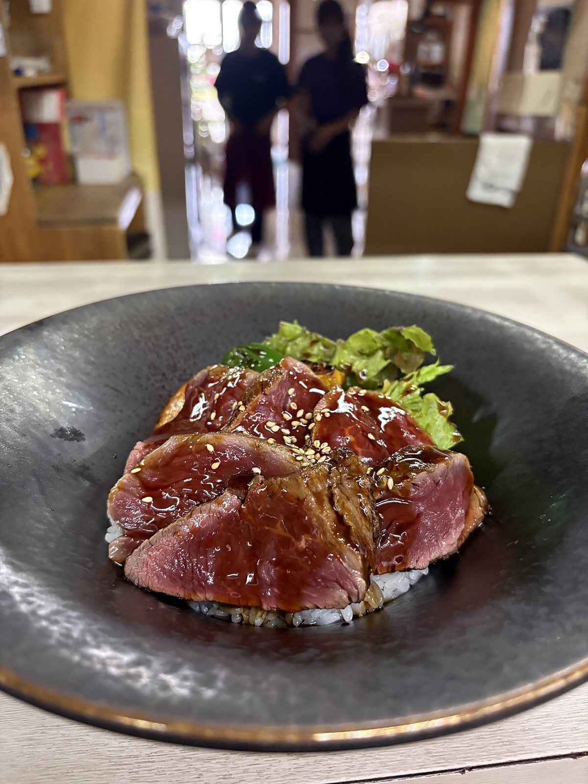 豊南焼肉の豊南のレアステーキ丼。黒い丼にレアに焼いた和牛ステーキを並べ、ステーキソースをかけた丼
